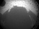 This is one of the first images taken by NASA's Curiosity rover, which landed on Mars the evening of August 5 (PDT). It was taken through a "fisheye" wide-angle lens on one of the rover's front Hazard-Avoidance cameras at one-quarter of full resolution. The camera is the left eye of a stereo pair positioned at the middle of the rover's front side. The clear dust cover on the camera is still on in this view, and dust can be seen around its edge, along with three cover fasteners. The rover's shadow is visible in the foreground. [Photo courtesy of NASA/JPL-Caltech]

